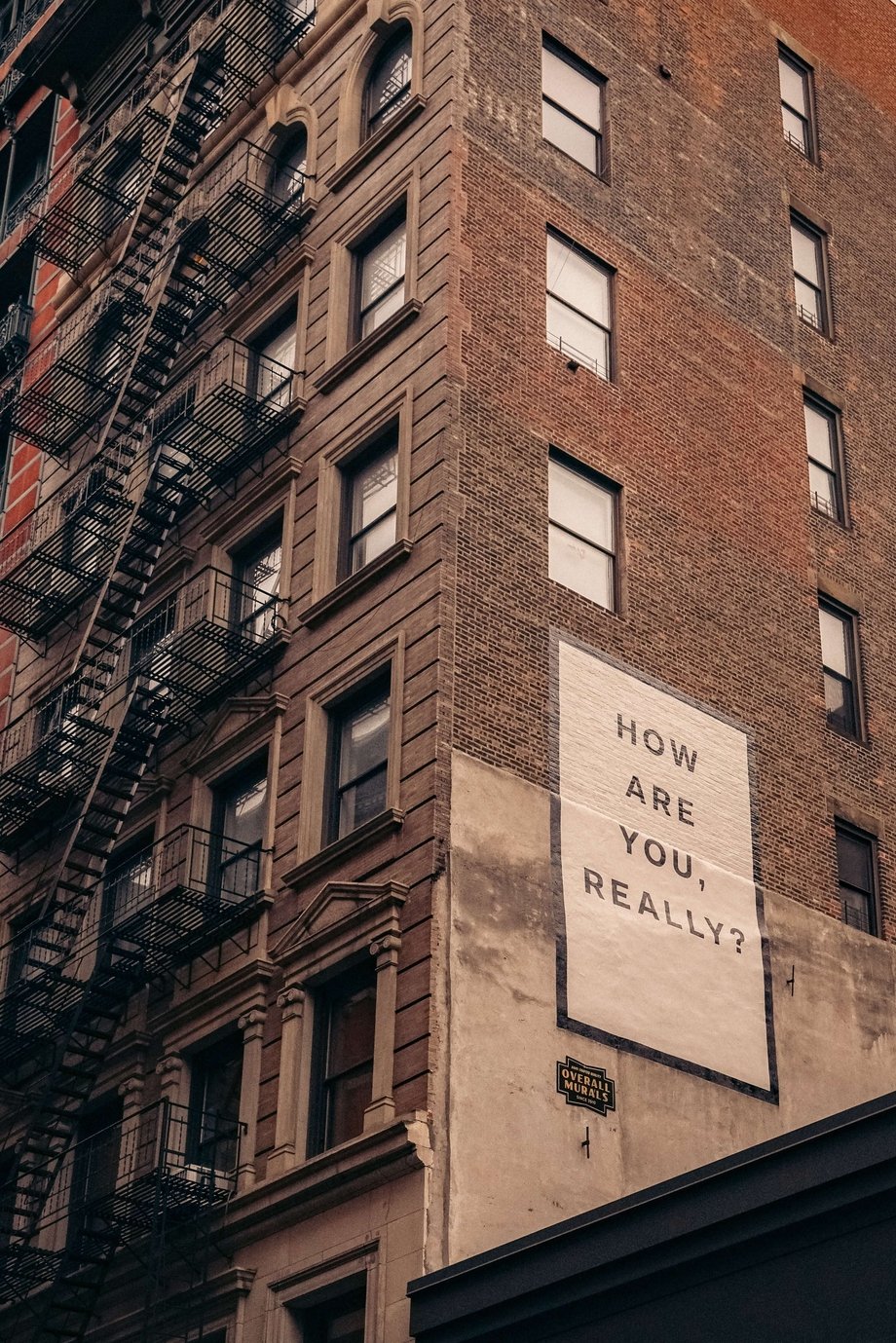 The exterior of a brick building, on the side of which a sign reads "How Are You Really?"