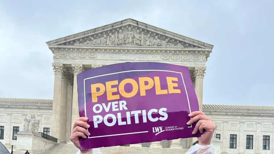 Hands holding purple and gold sign that reads "PEOPLE OVER POLITICS" in front of the US Supreme Court Building