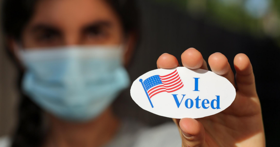 Woman in mask holding "I voted" sticker